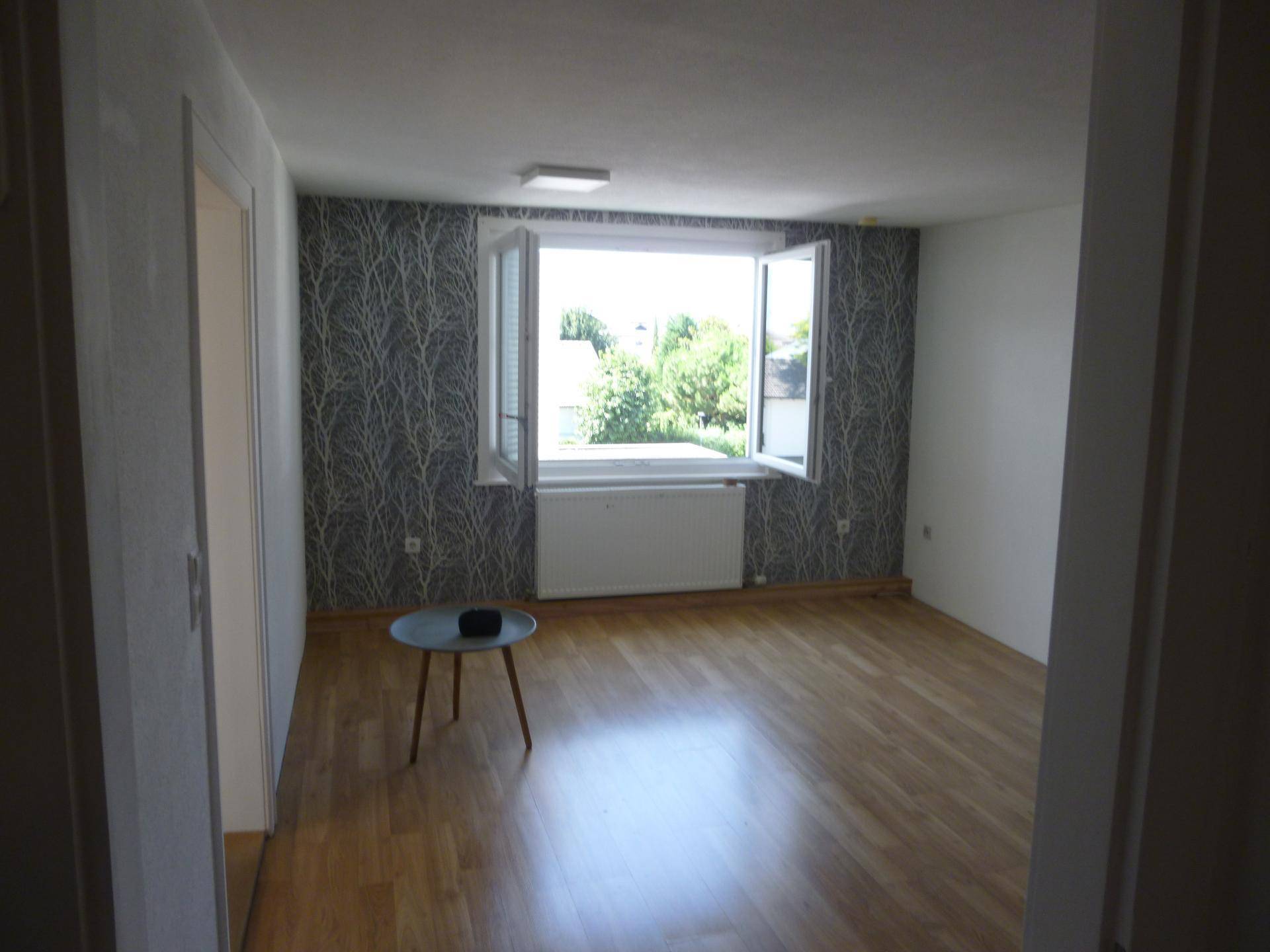 Geräumiges Zimmer mit Laminatboden und einer gemusterten Tapetenwand, bietet viel Licht.