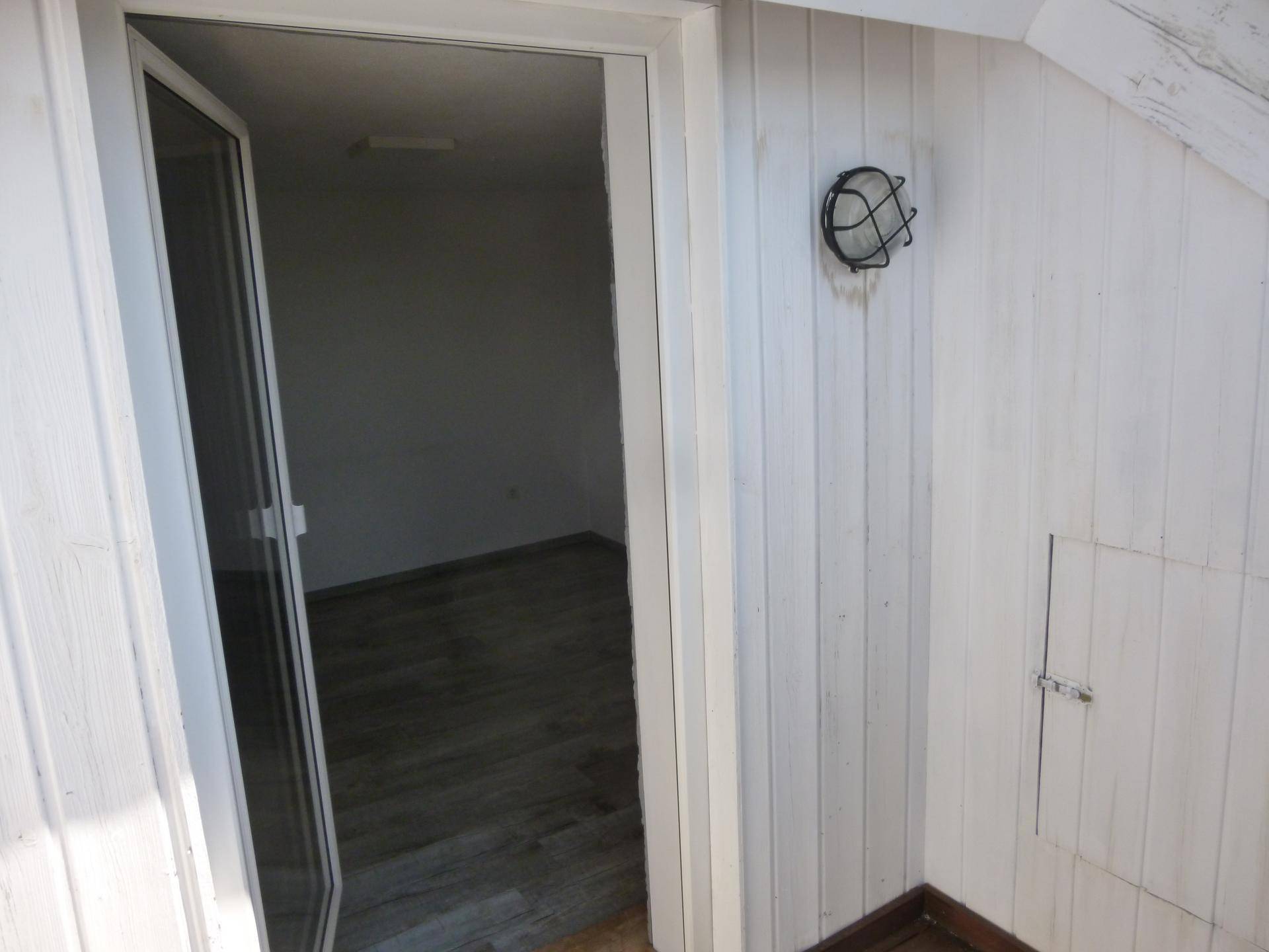 Türöffnung zu einem hellen Raum mit Holzverkleidung an der Wand und einer Wandleuchte.