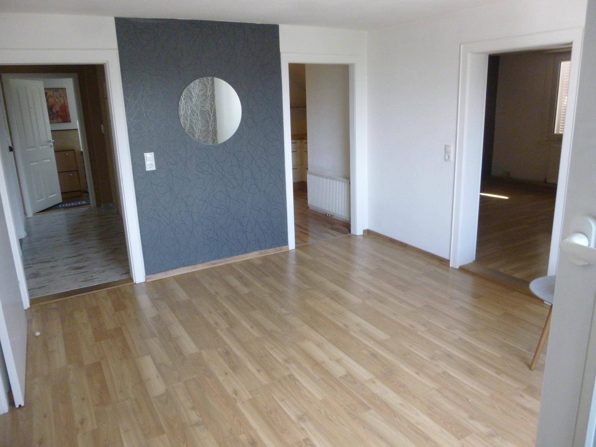 Heller Wohnraum mit Laminatboden und einer dunkelgrauen Akzentwand mit Spiegel.