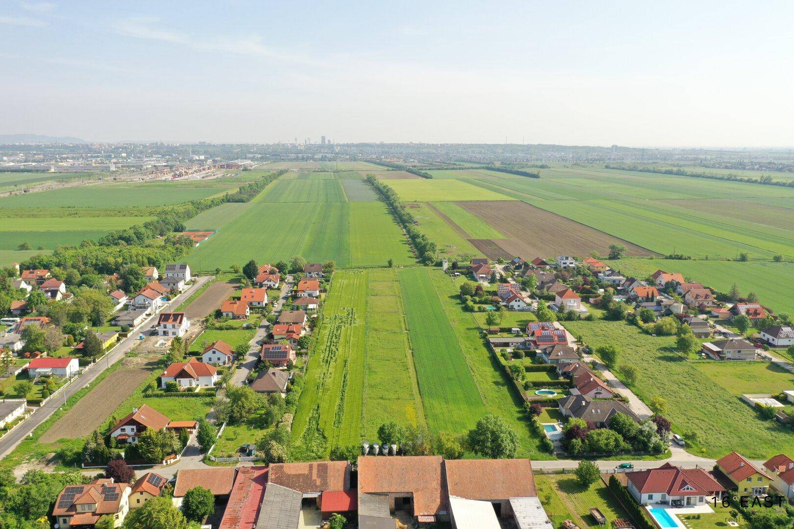 Weitläufige Luftaufnahme einer Wohngegend mit weiten Feldern und einer Stadt in der Ferne.
