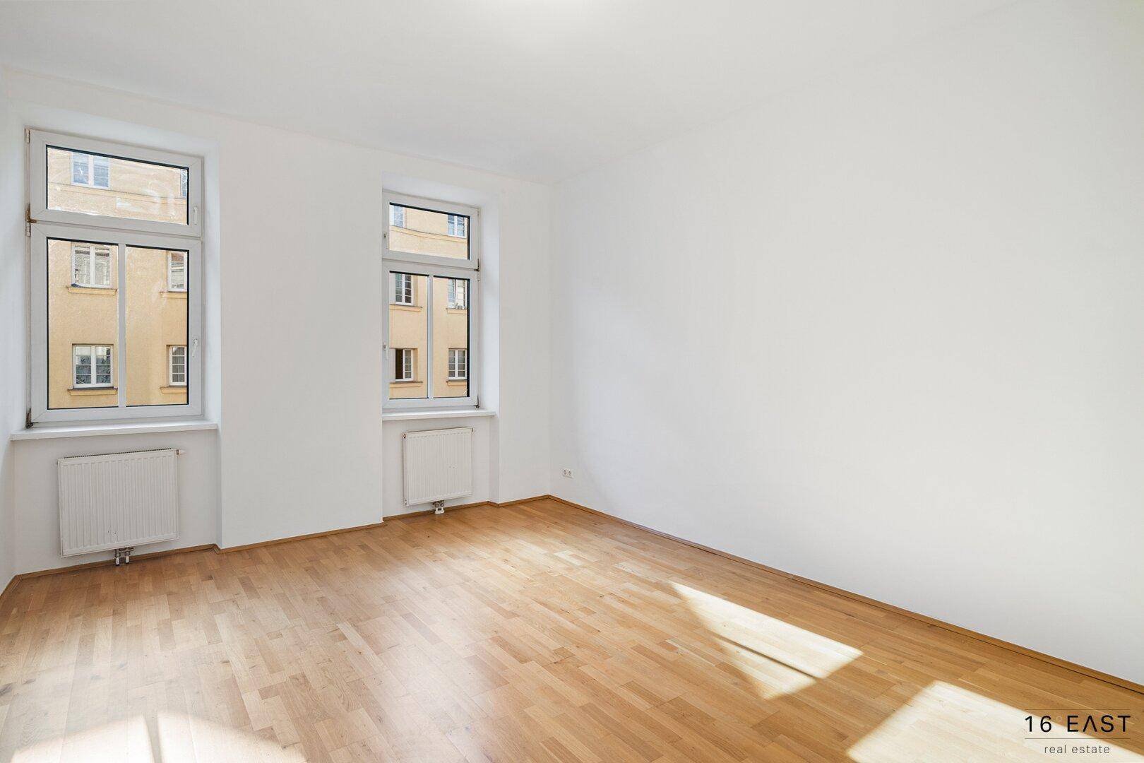 Helles Zimmer mit Parkettboden und zwei Fenstern, ideal als Wohn- oder Schlafzimmer nutzbar.