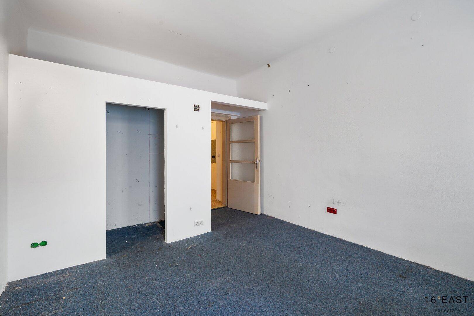 Leeres Zimmer mit Teppichboden und einer Nische, die für einen Einbauschrank vorgesehen ist.
