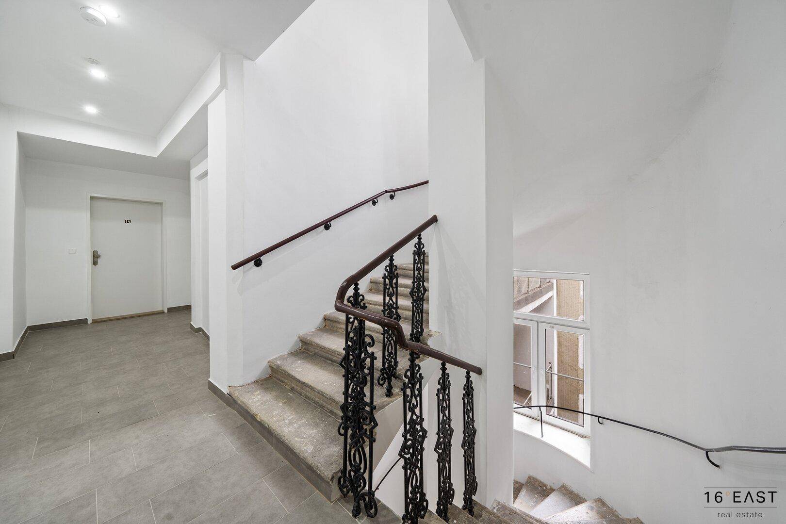 Historisches Treppenhaus mit schmiedeeisernem Geländer und Fliesenboden.