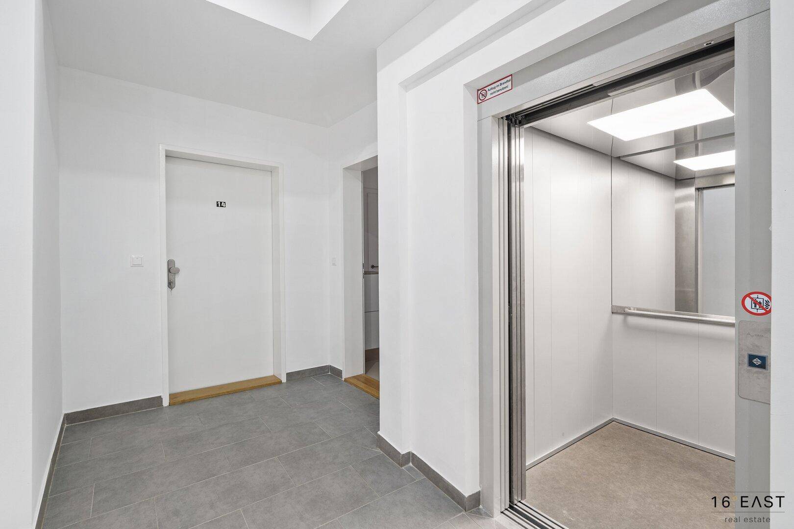 Heller Flur mit offenem Aufzug und modernen Fliesen auf dem Boden.