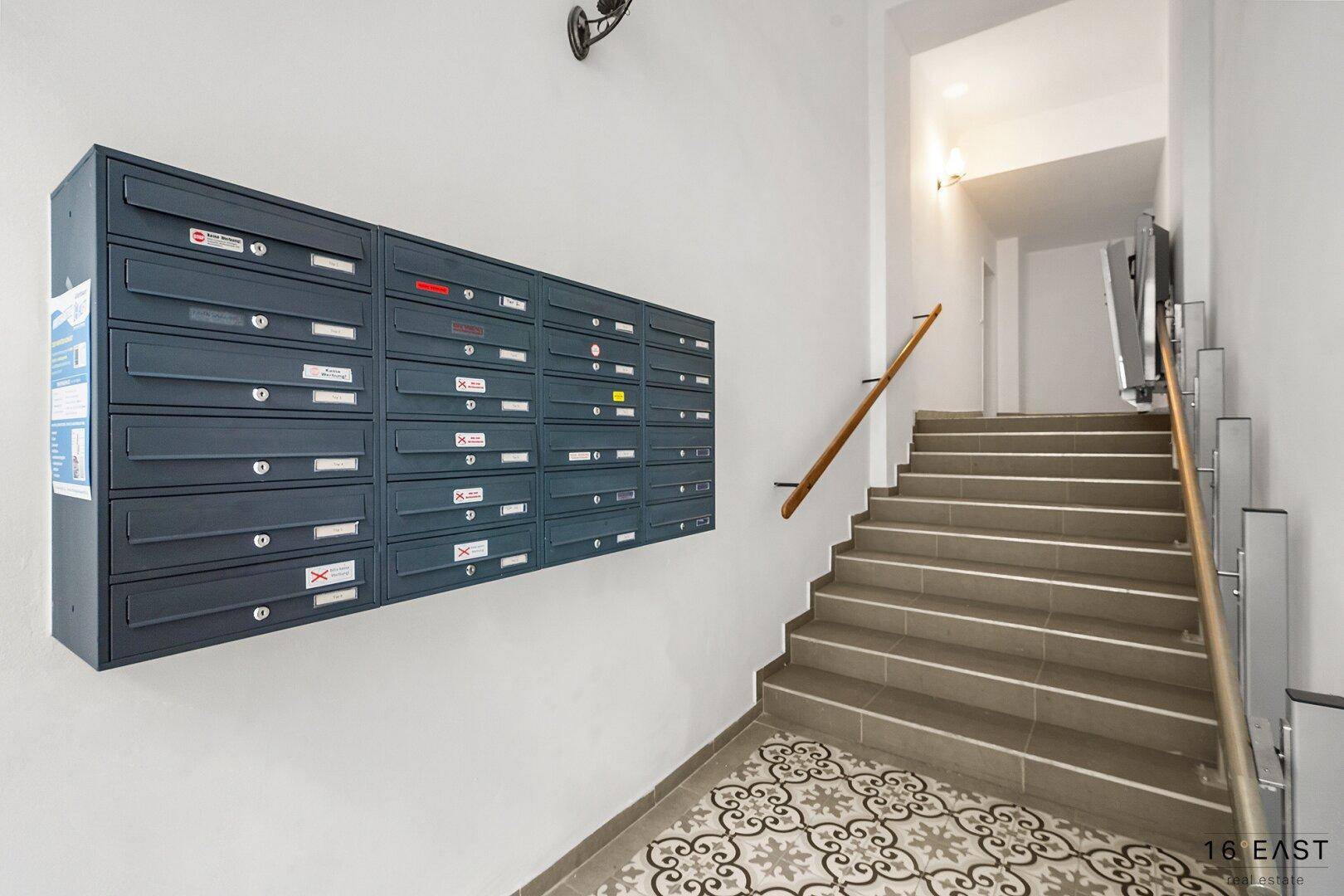 Eingangsbereich mit Briefkästen, gemusterten Fliesen und Treppenaufgang in einem Mehrfamilienhaus.