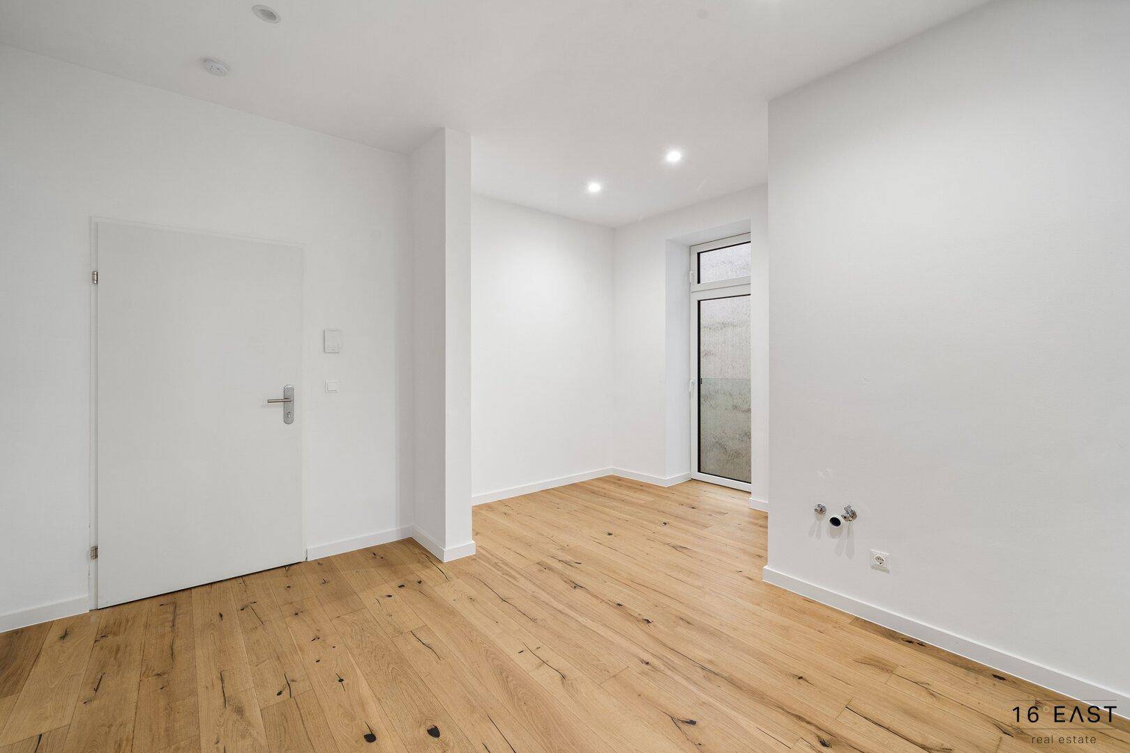 Heller Raum mit Holzboden und Zugang zu einem kleinen Außenbereich, ideal für verschiedene Nutzungen.