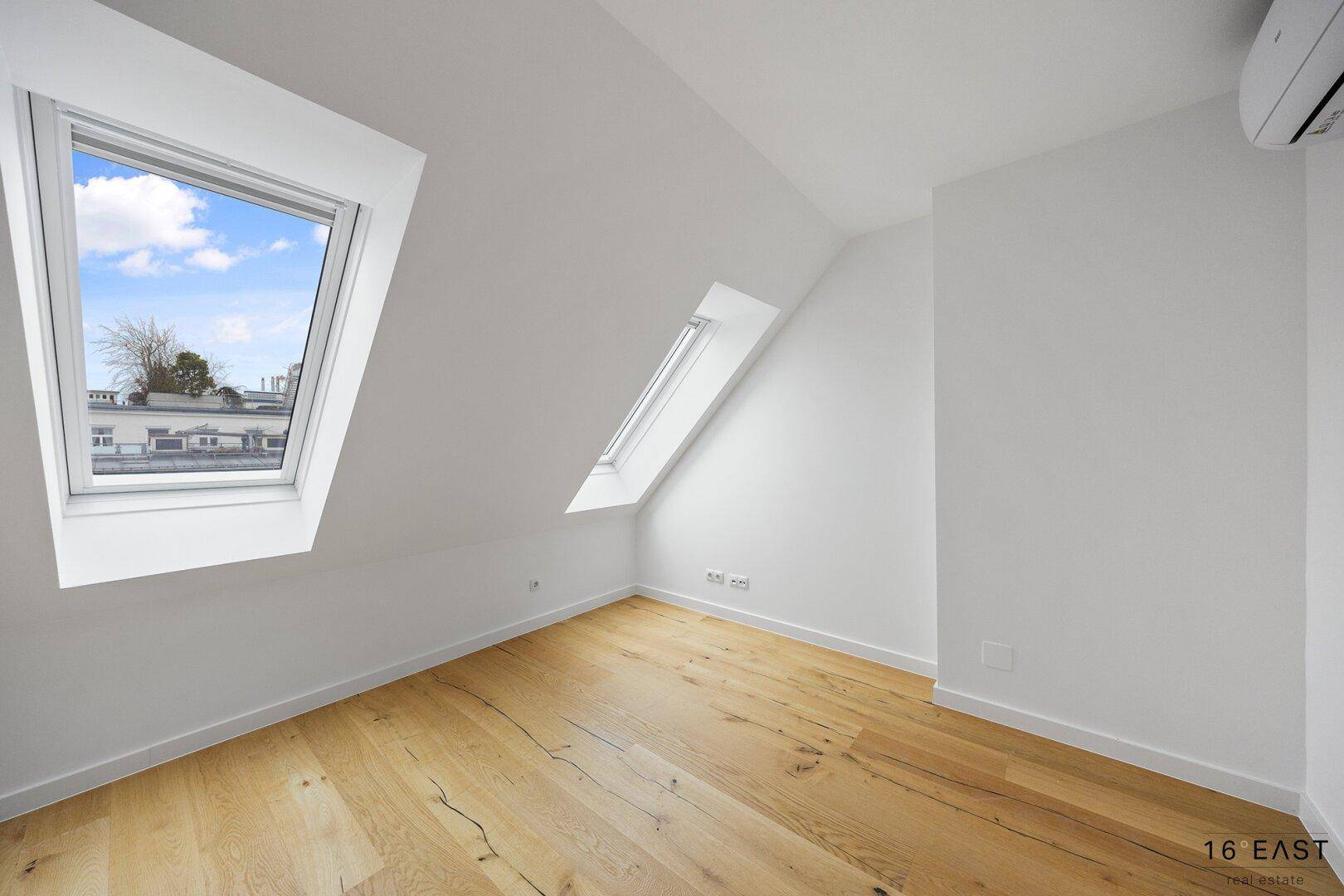 Helles Schlafzimmer mit Holzboden, Dachschrägen und zwei Dachfenstern, ausgestattet mit Klimaanlage.