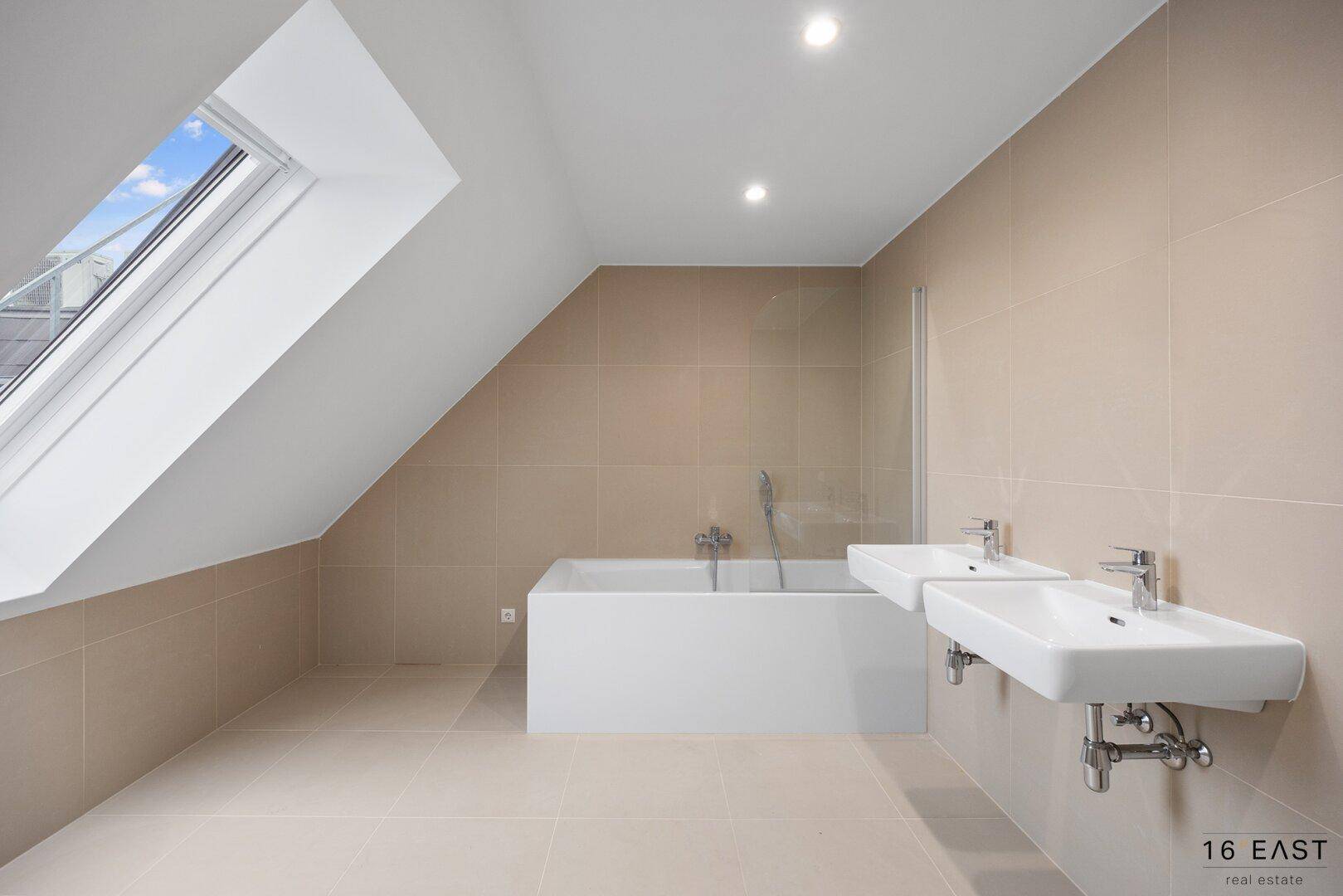 Modernes Badezimmer mit Badewanne, Doppelwaschbecken und großem Dachfenster für viel Tageslicht.