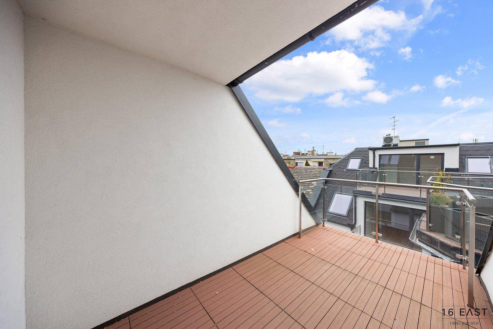 Geräumiger Balkon mit Holzboden und Glasgeländer, bietet einen weiten Blick über die Dächer.