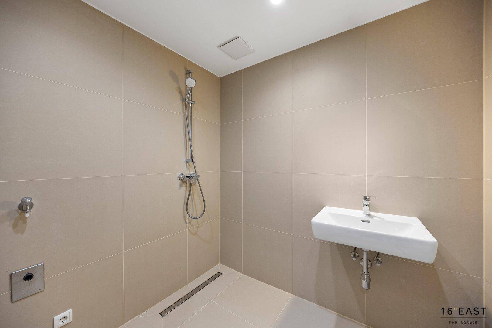 Modernes Badezimmer mit ebenerdiger Dusche und Einzelwaschbecken, komplett gefliest in neutralen Tönen.