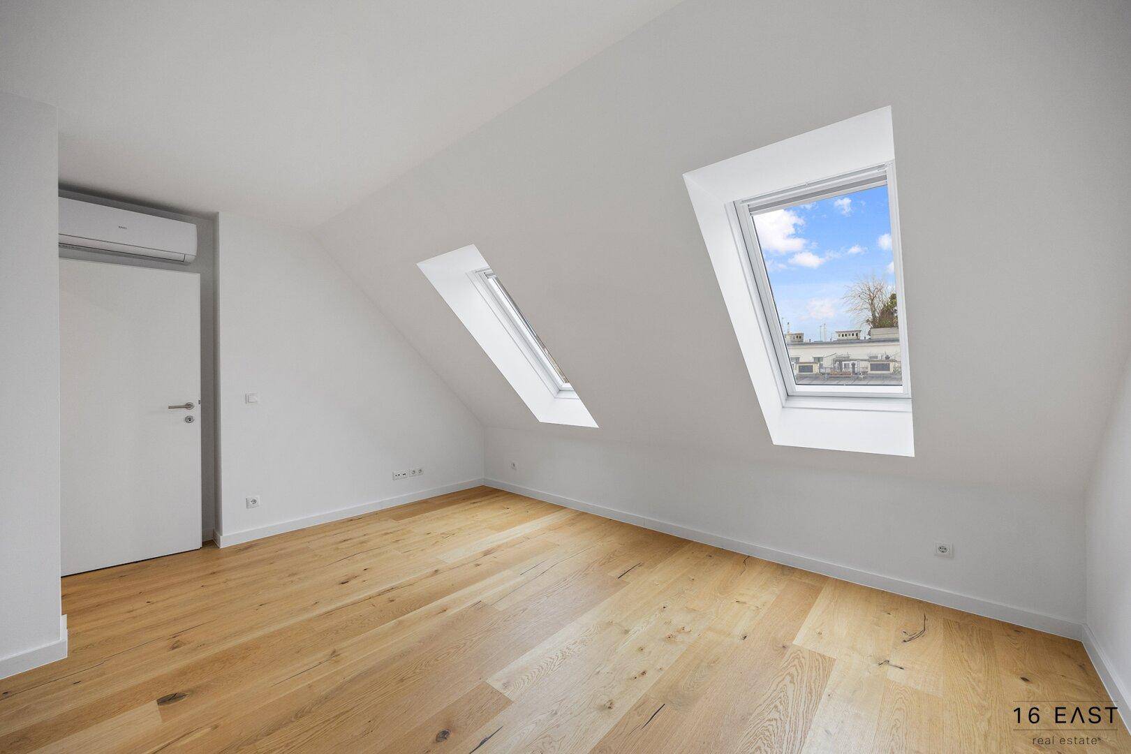 Helles Schlafzimmer mit Holzboden, Dachschrägen und zwei Dachfenstern, ausgestattet mit Klimaanlage.