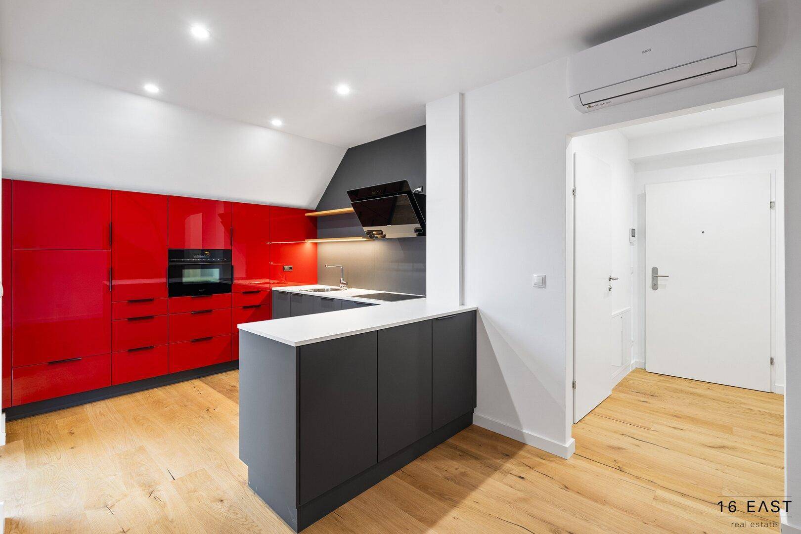 Moderne Einbauküche in Rot und Grau mit integrierten Geräten und Zugang zum Flur.