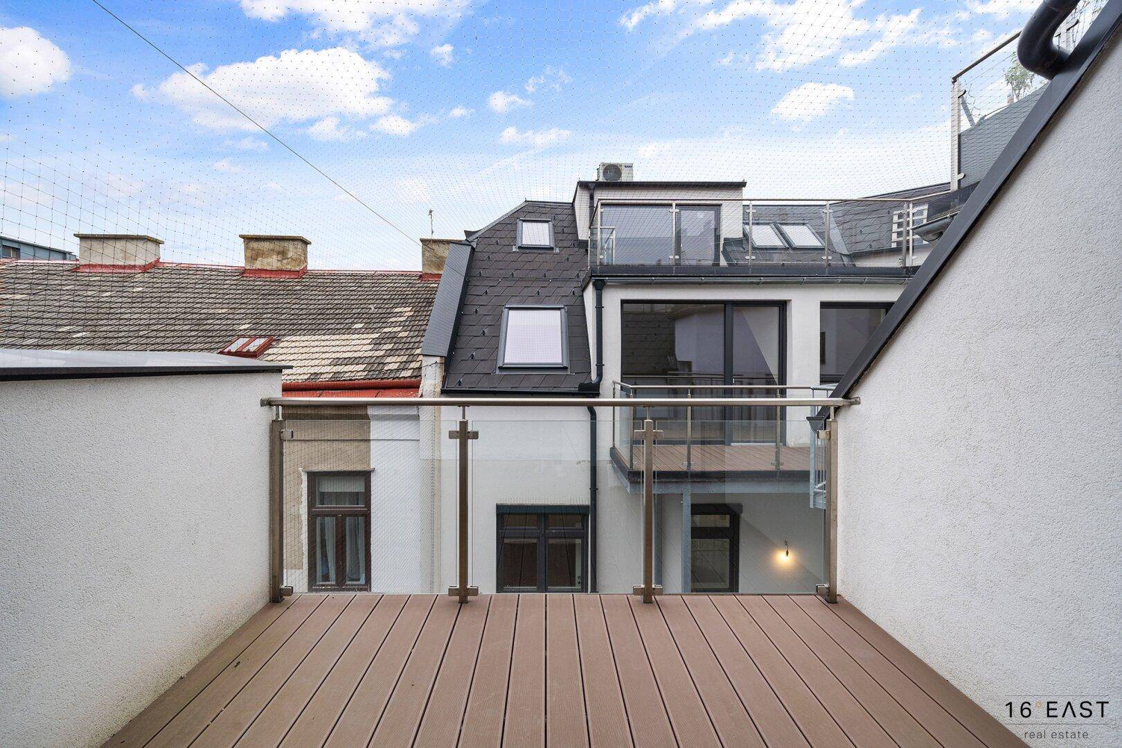 Balkon mit Glasgeländer und Blick auf die umliegenden Dächer und Gebäude.