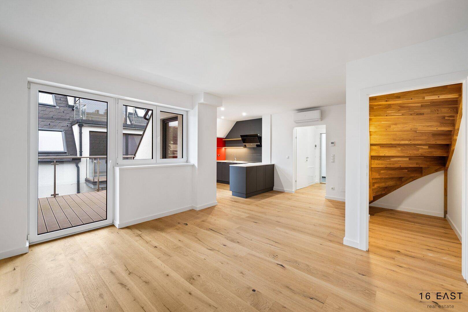 Geräumiger offener Wohnbereich mit Holzboden, Balkonzugang und einer eleganten Holztreppe.