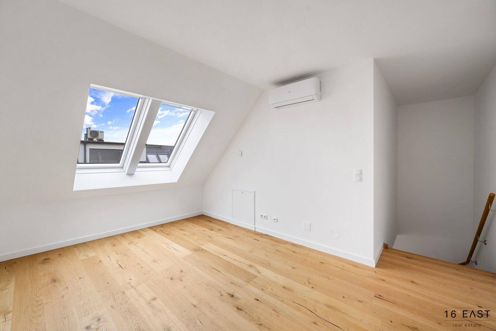 Helles Schlafzimmer im Dachgeschoss mit schrägen Wänden, Dachfenstern und Klimaanlage.