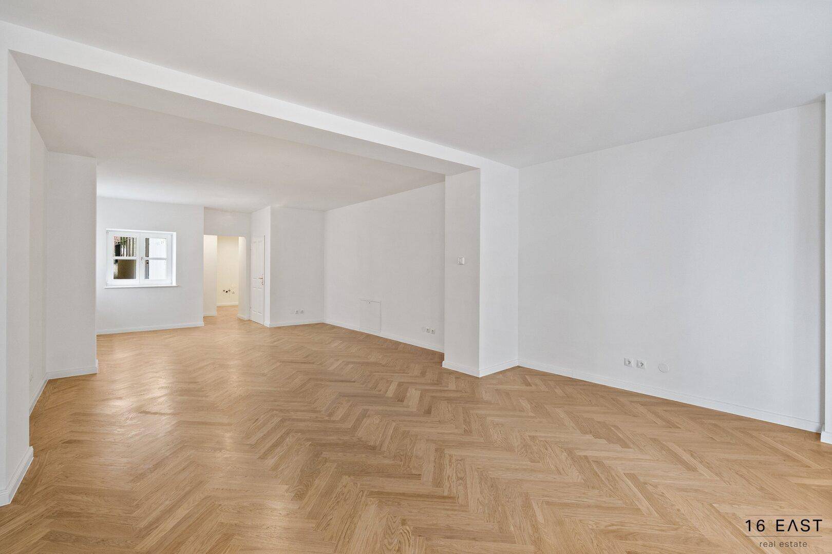 Geräumiger, heller Bürobereich mit elegantem Fischgrätparkett und weißen Wänden.