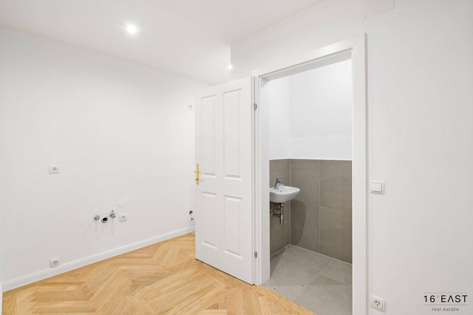 Vorbereitungsraum mit Fischgrätparkett und Zugang zu einer modernen Gästetoilette.