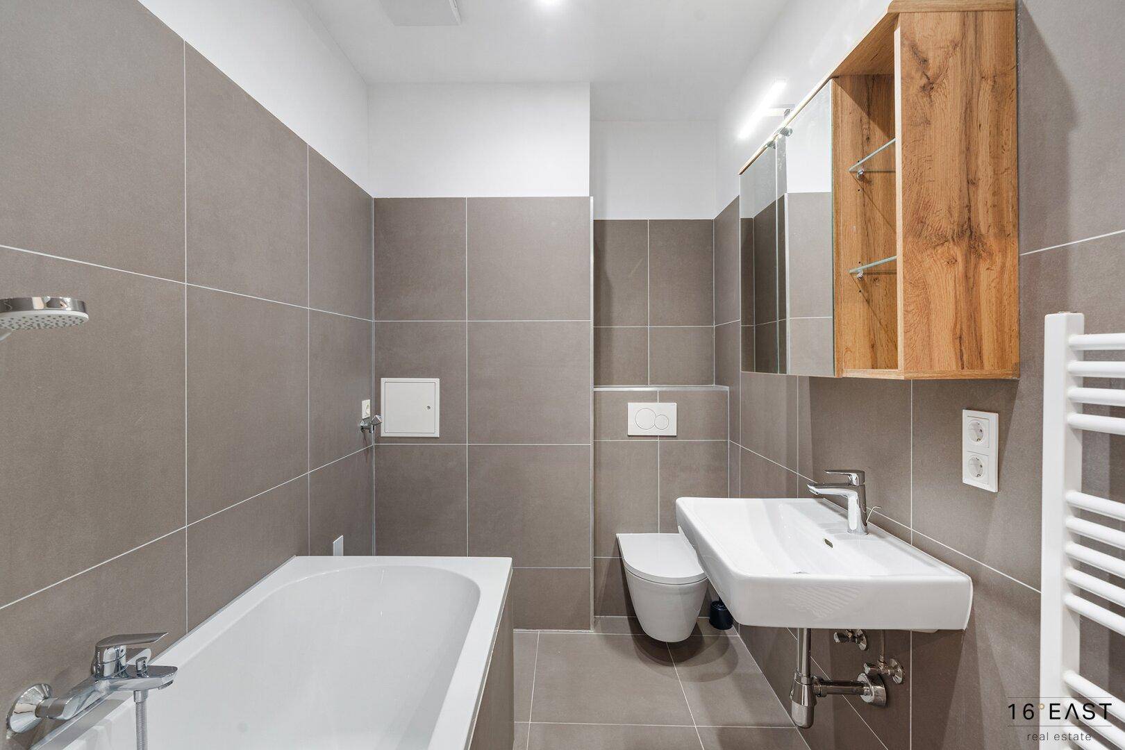 Modernes Badezimmer mit Badewanne, Dusche, WC und Waschbecken, ausgestattet mit grauen Fliesen.