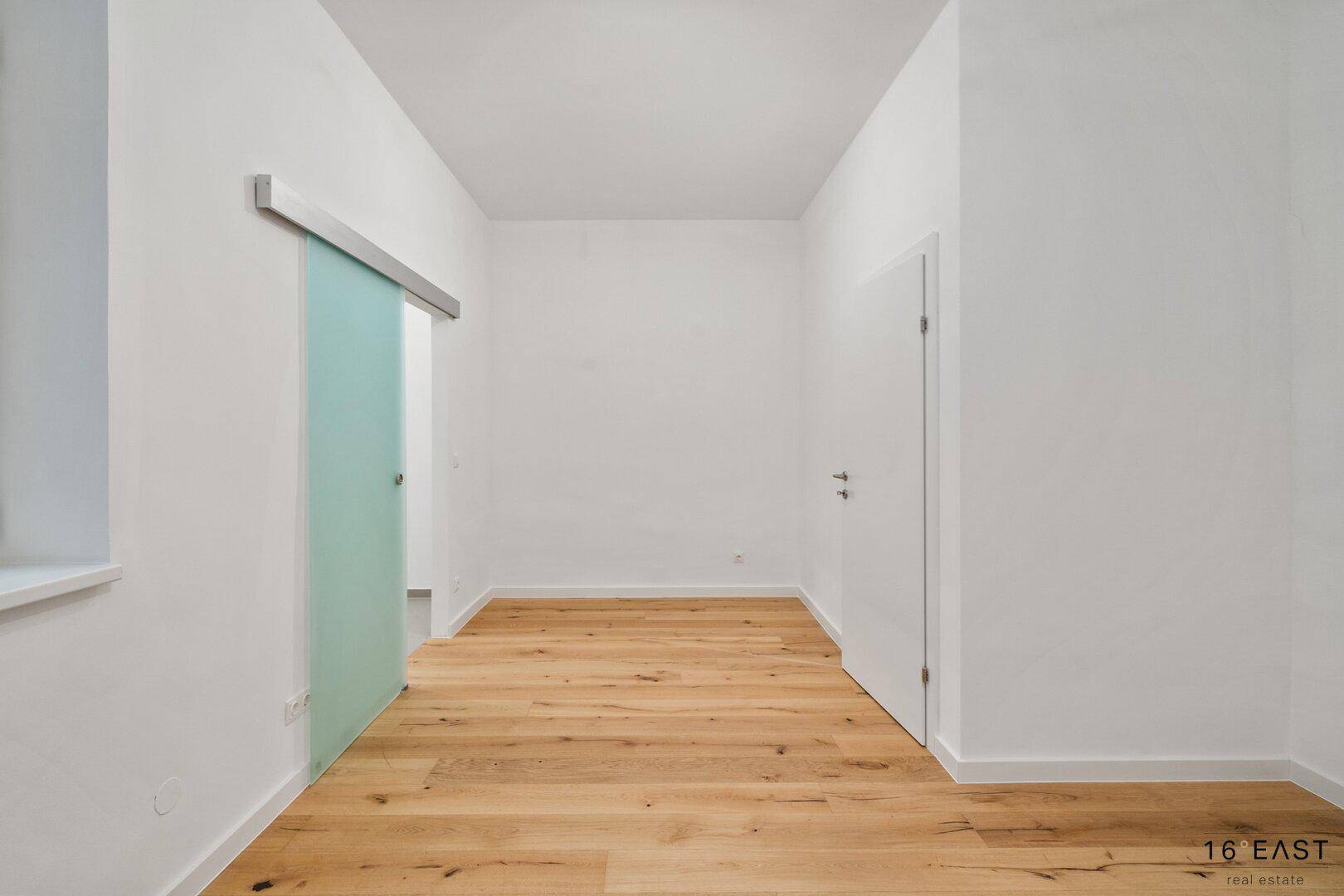 Heller Raum mit Holzboden und einer modernen Glasschiebetür.