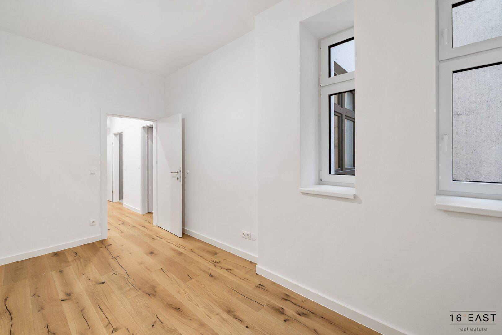 Leeres Zimmer mit Holzboden und Blick in den Flur, bereit zur individuellen Gestaltung.