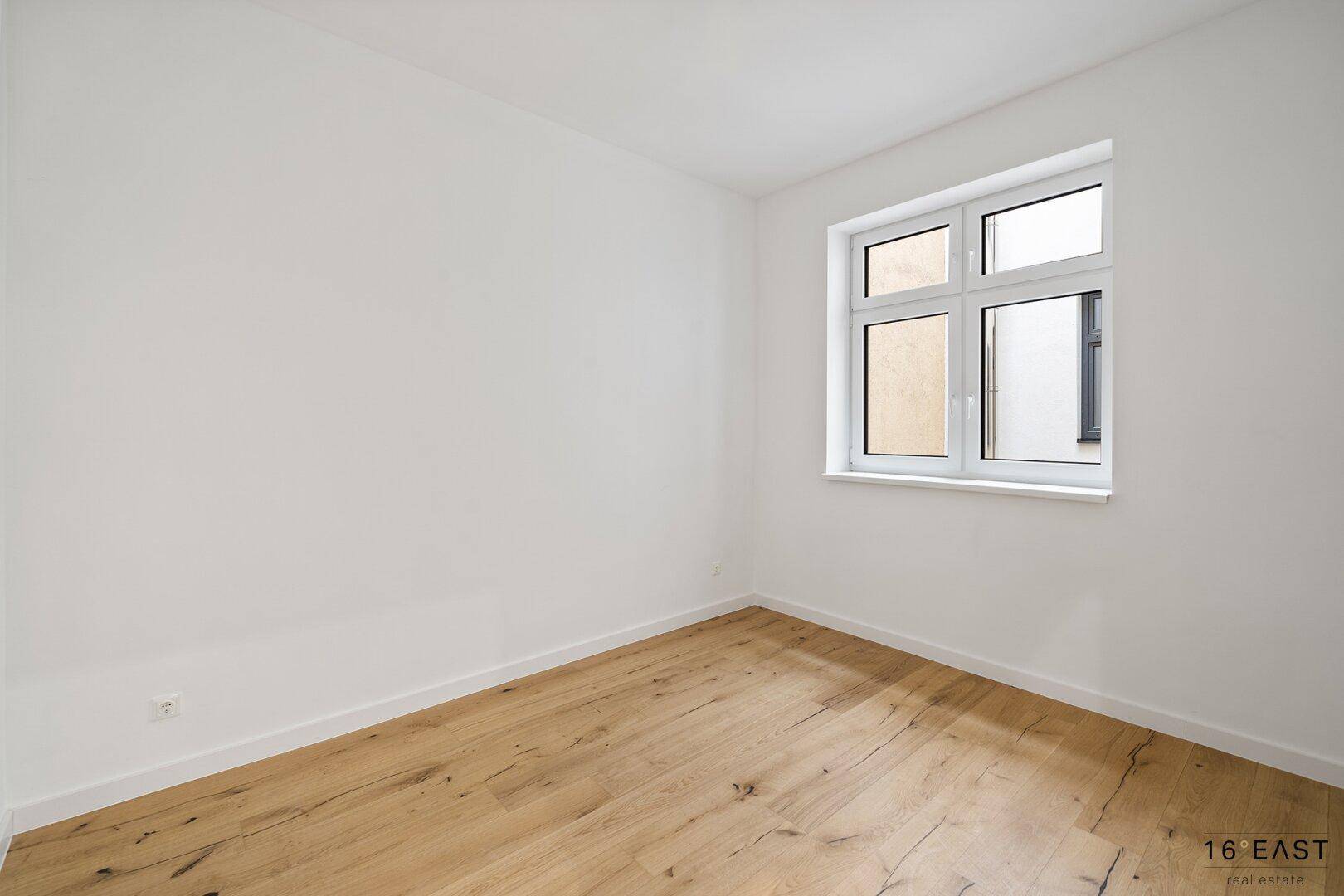 Kleineres, helles Zimmer mit Holzboden und einem großen Fenster, ideal als Schlafzimmer.
