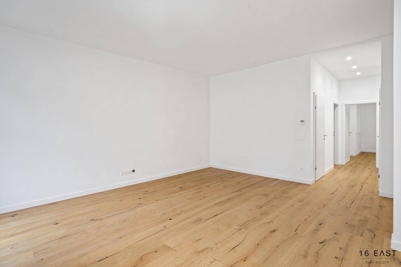 Heller Raum mit Holzboden und Zugang zu einem modernen Flur mit Einbaustrahlern.