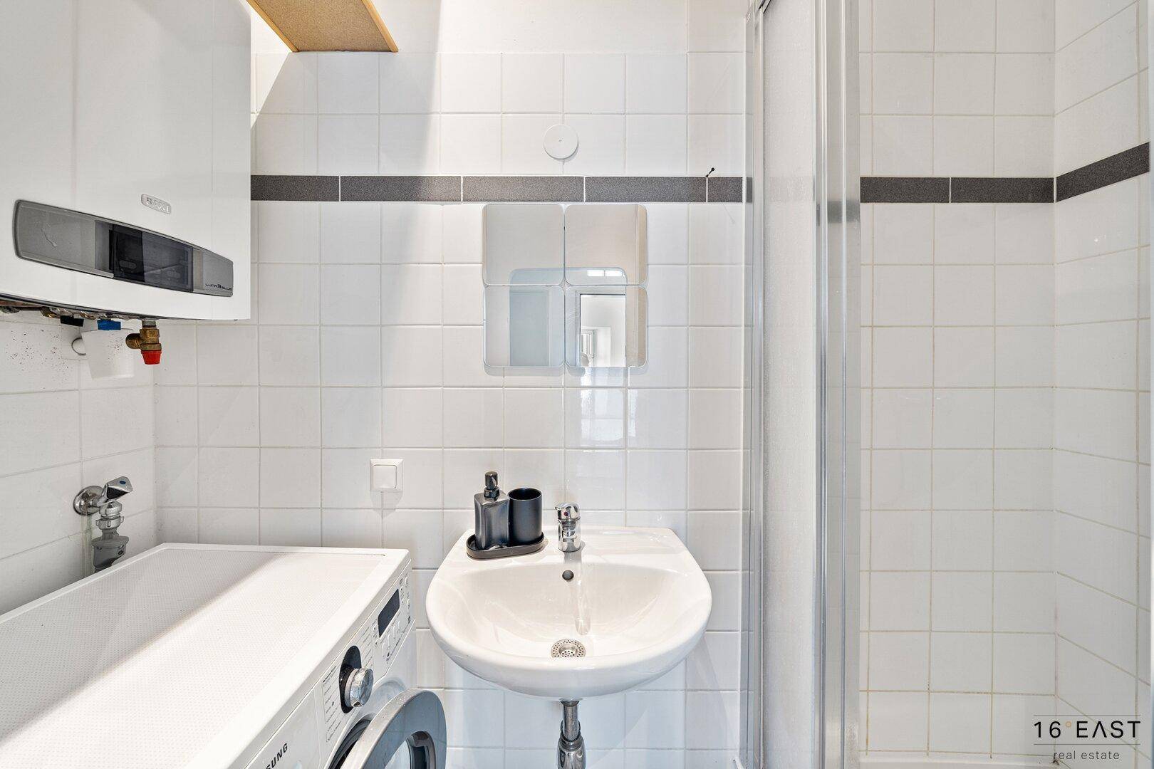 Modernes Badezimmer mit weißen Fliesen, Dusche und Waschmaschine.