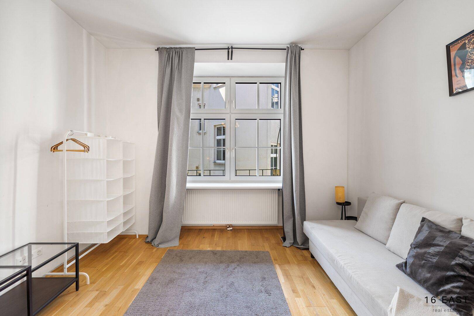 Gemütliches Schlafzimmer mit Holzboden, Vorhängen und einem Kleiderständer.