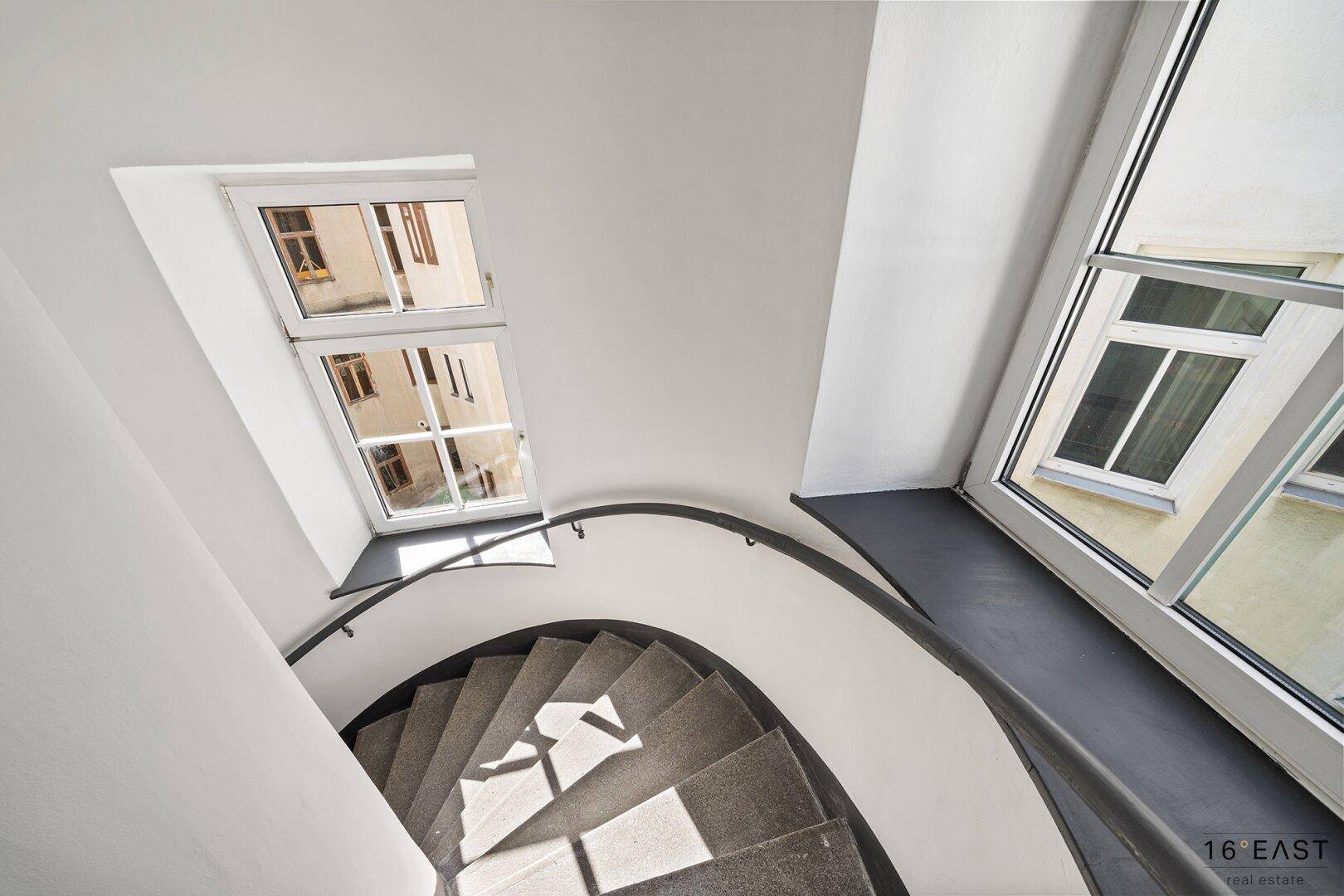 Wendeltreppe im Treppenhaus mit großen Fenstern, die viel Licht hereinlassen.