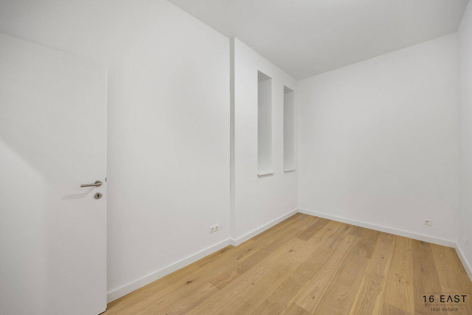 Leerer Raum mit hellem Holzfußboden und weißen Wänden, bereit zur individuellen Gestaltung.