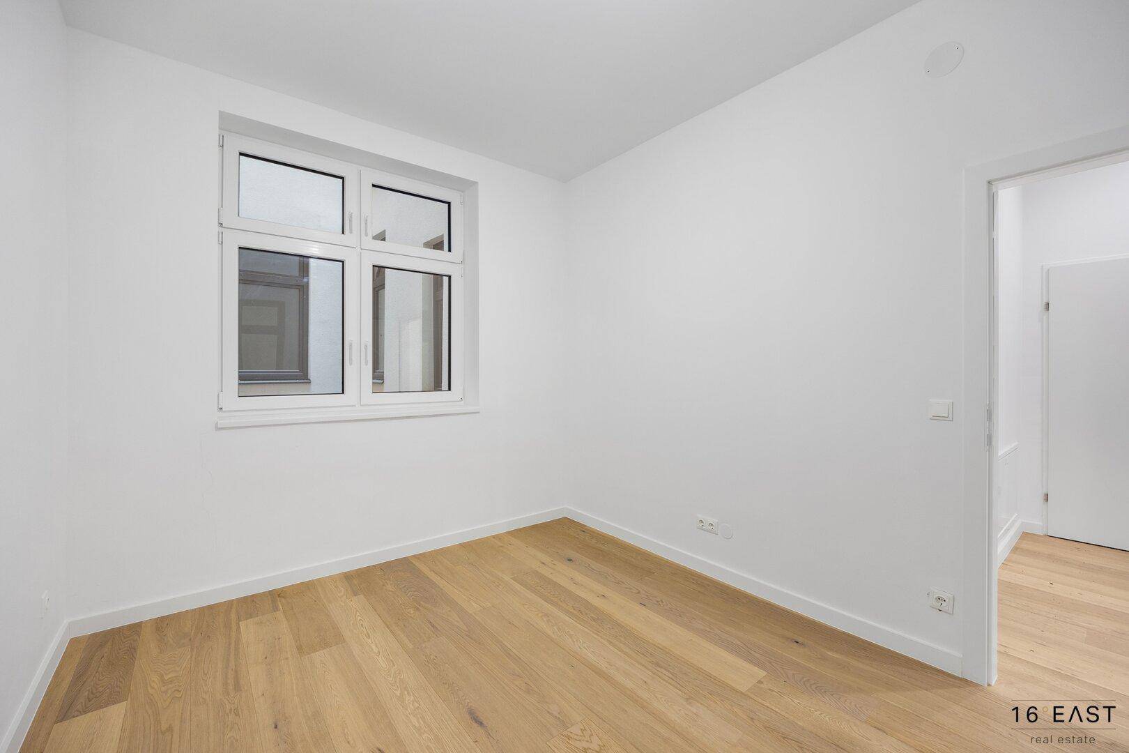 Heller, leerer Raum mit einem Fenster und Holzfußboden, ideal für ein Schlafzimmer oder Büro.