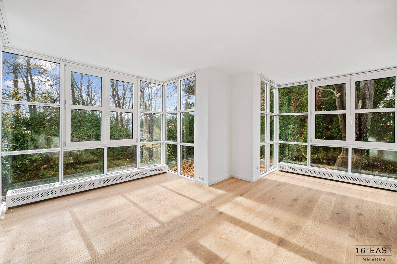 Geräumiges Wohnzimmer mit großen Fenstern, die viel Tageslicht hereinlassen und einen grünen Ausblick bieten.
