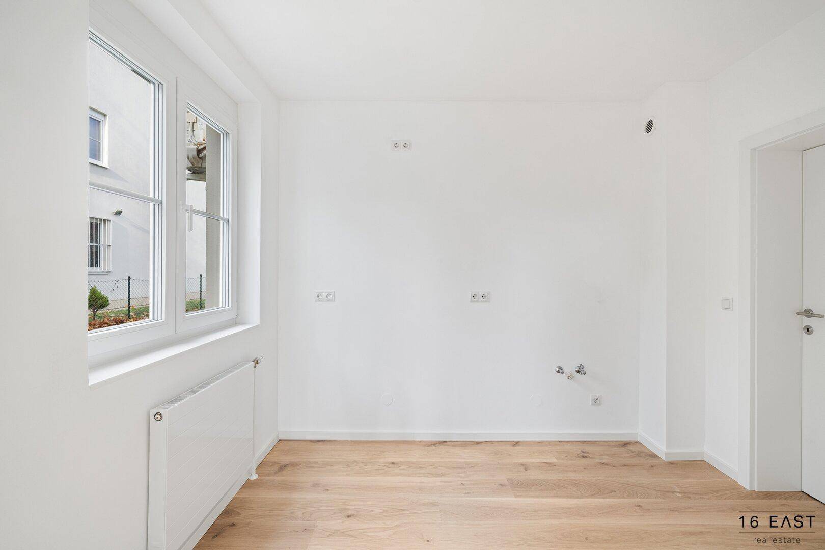 Leerer Küchenraum mit Anschlüssen für eine Einbauküche und Fenster.