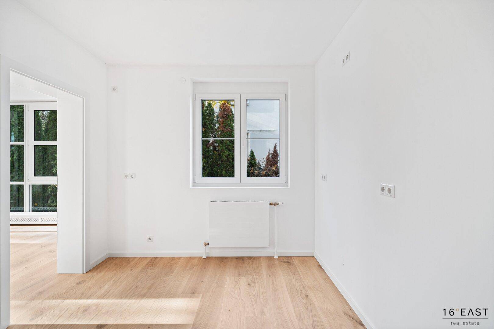 Helles Zimmer mit Holzboden und Fenster, das einen Blick ins Grüne bietet.