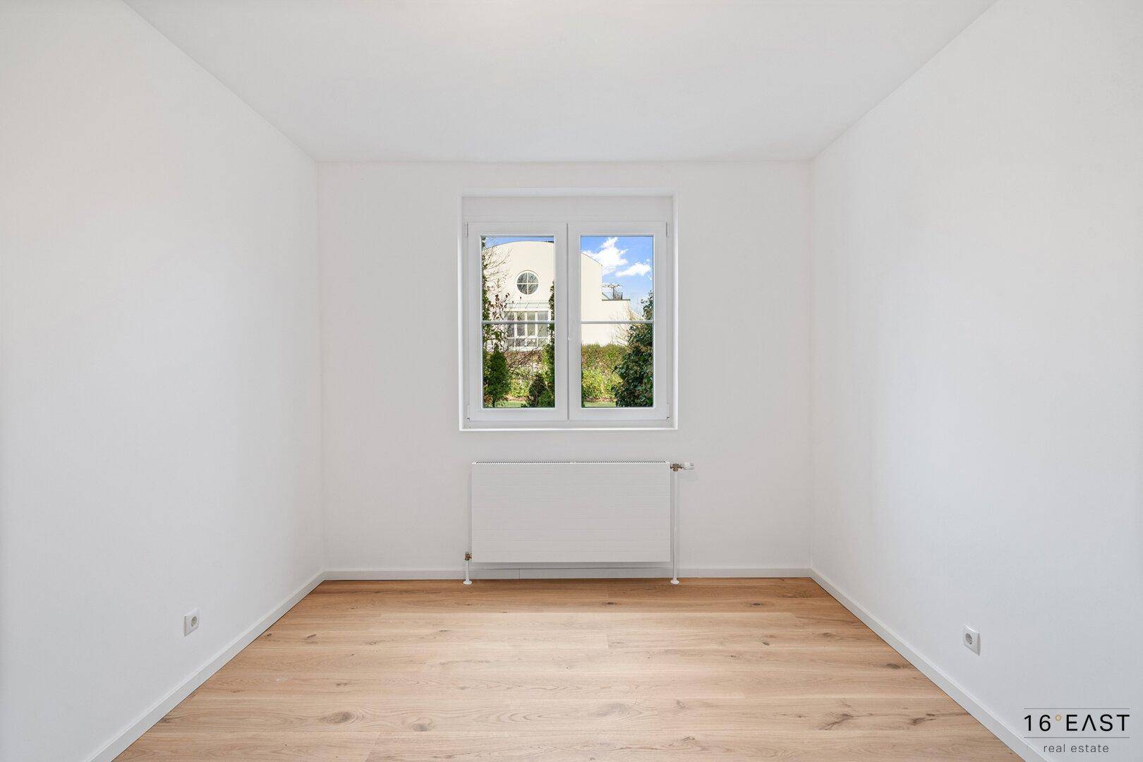 Helles Schlafzimmer mit Holzboden und Fenster, das einen Blick auf die Umgebung bietet.