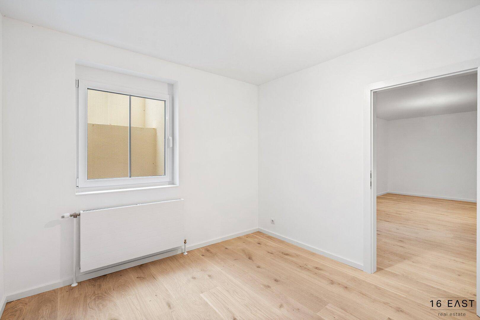 Helles Zimmer mit Holzboden und Fenster, das viel Tageslicht hereinlässt.