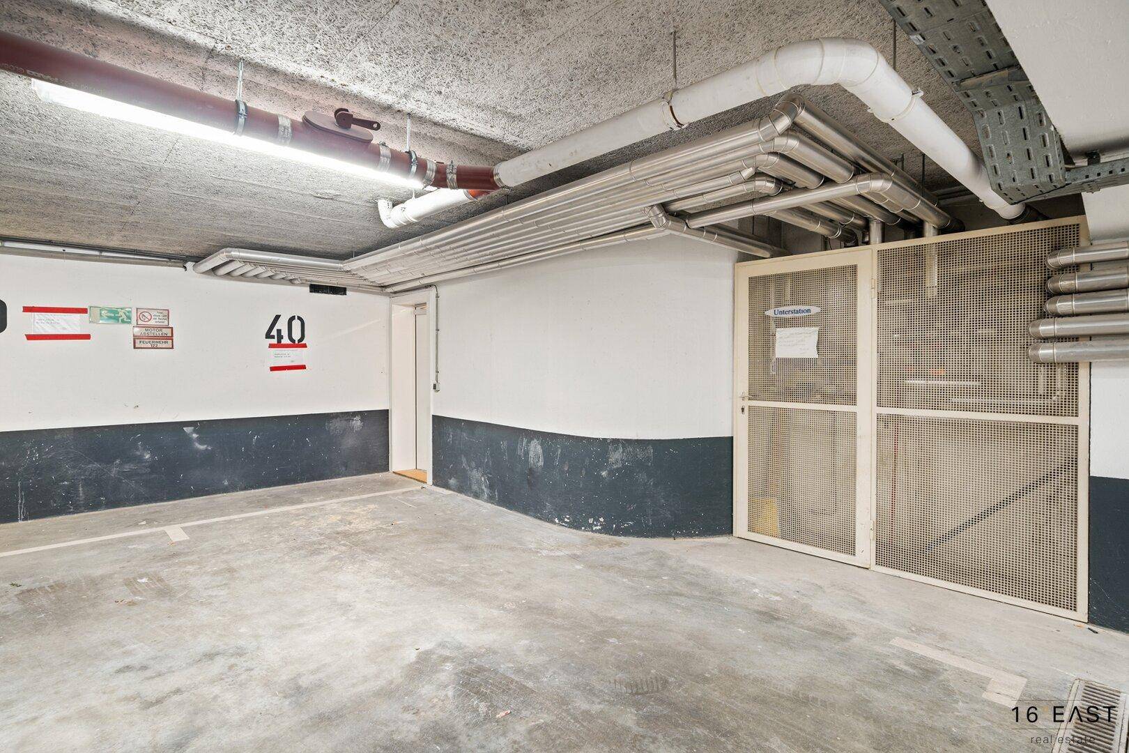 Tiefgaragenstellplatz mit Betonboden und sichtbaren Leitungen an der Decke.