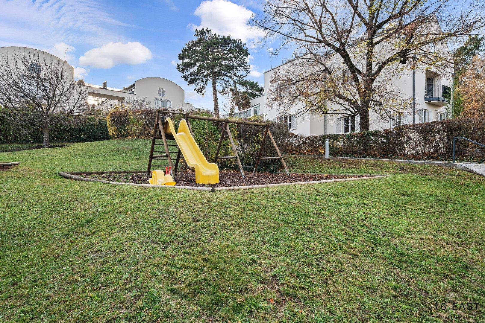Kinderspielplatz mit Rutsche und Schaukeln auf einer grünen Rasenfläche.