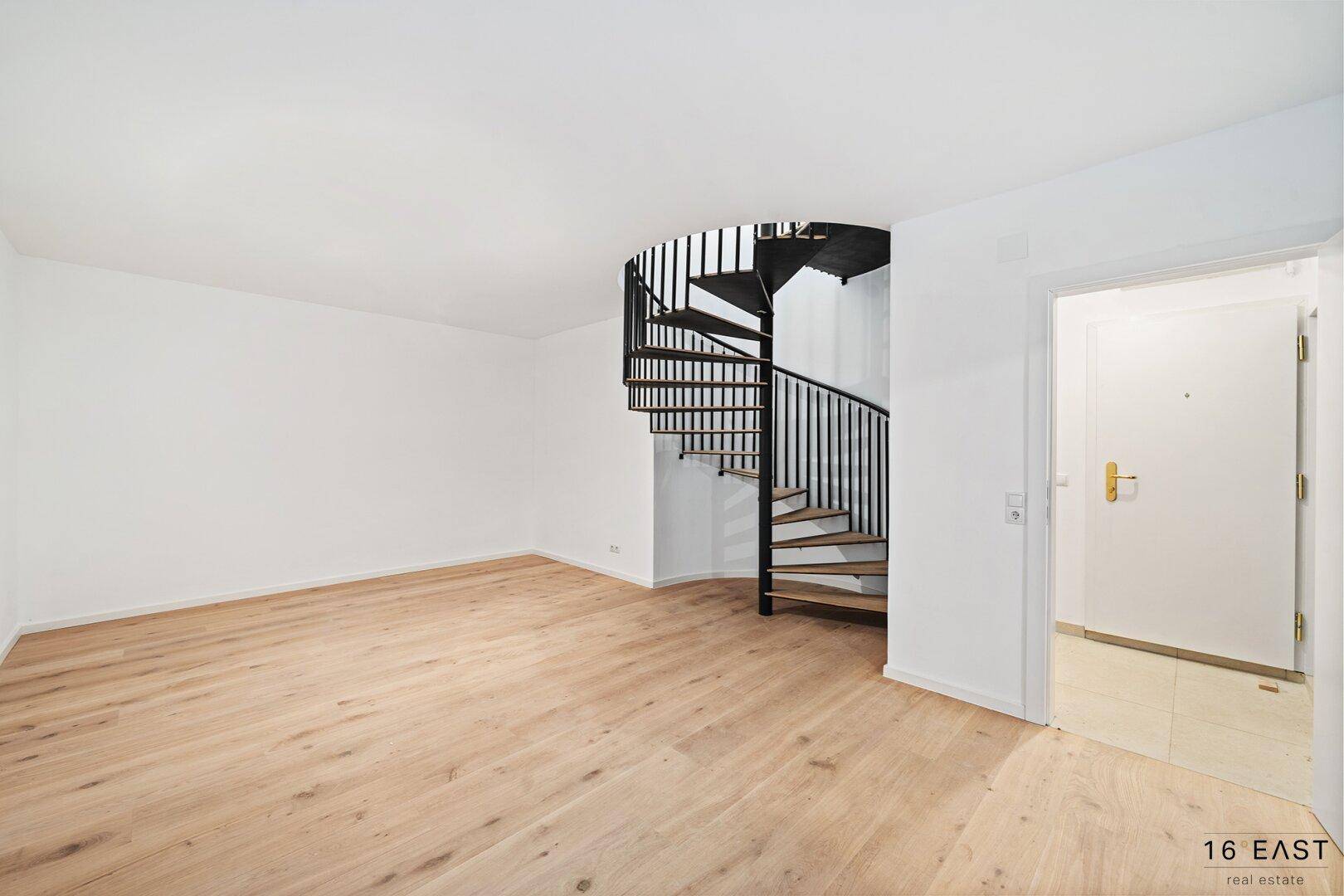 Geräumiger, heller Raum mit Holzboden und einer eleganten Wendeltreppe.