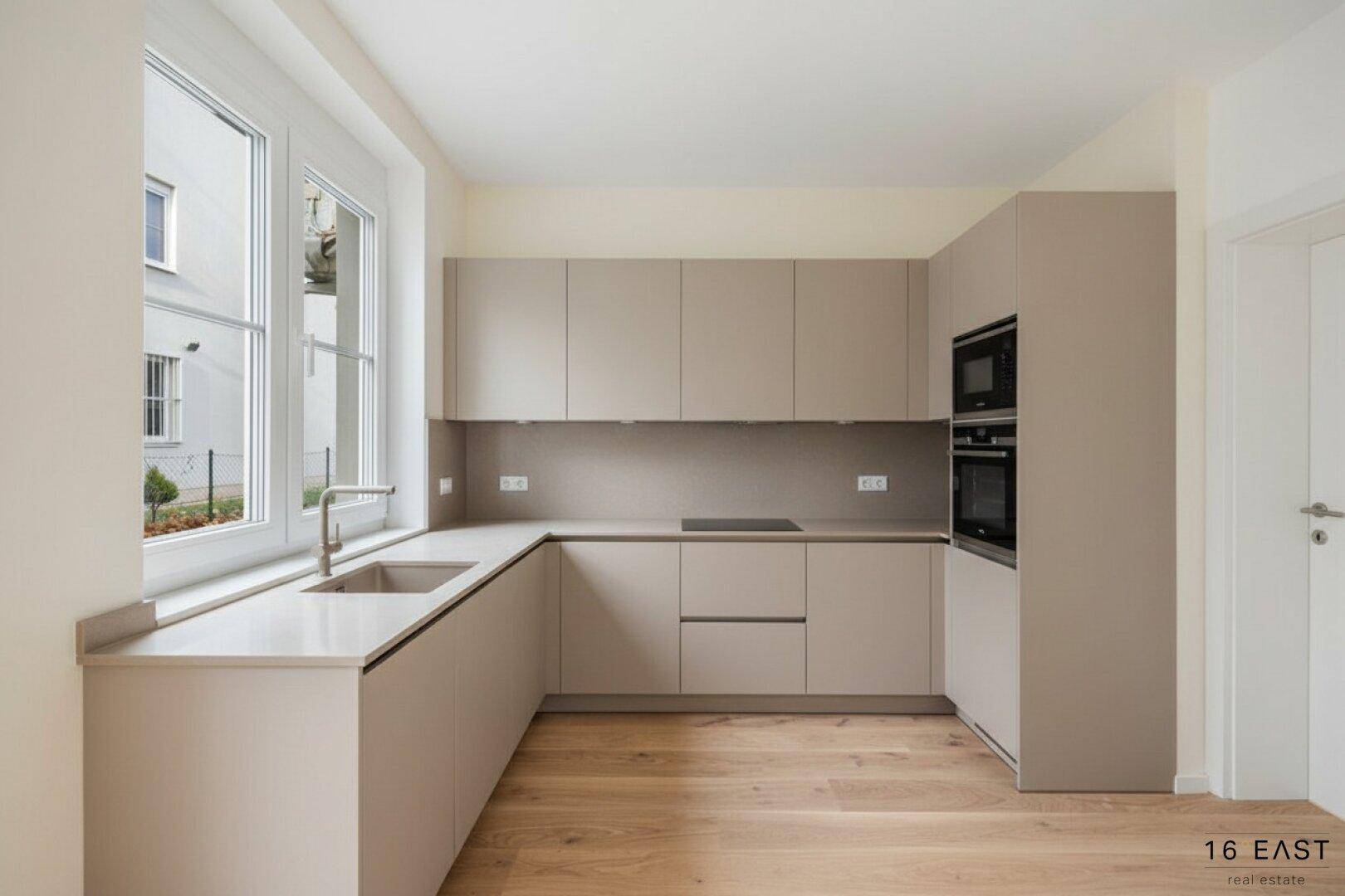 Moderne Einbauküche in U-Form mit beigen Schränken, integrierten Geräten und Holzboden.