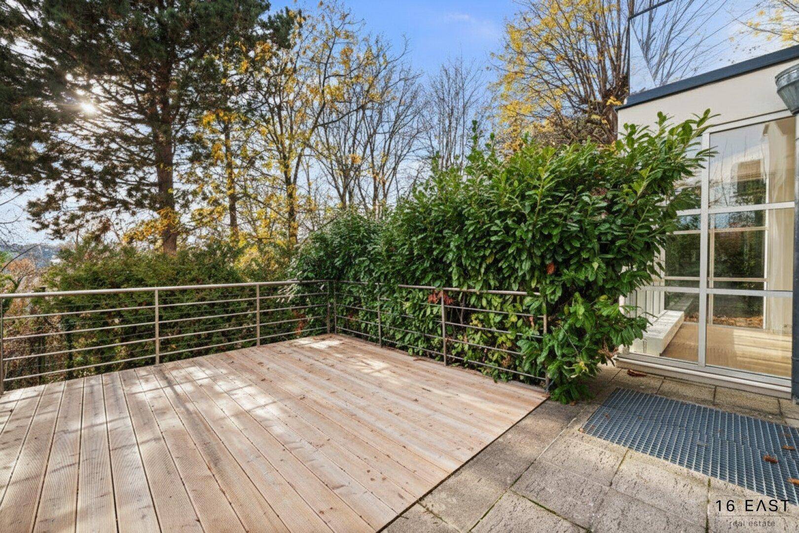 Geräumige Holzterrasse mit Metallgeländer und umgebender Hecke, ideal für Entspannung im Freien.