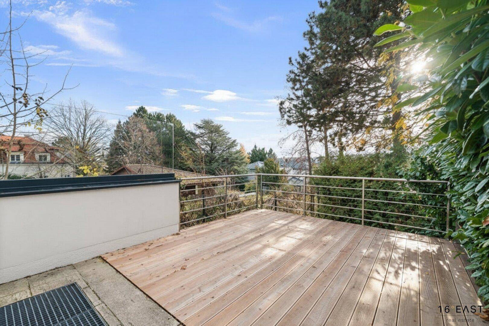 Unmöblierte Holzterrasse mit weitem Blick über die Umgebung und viel Grün.