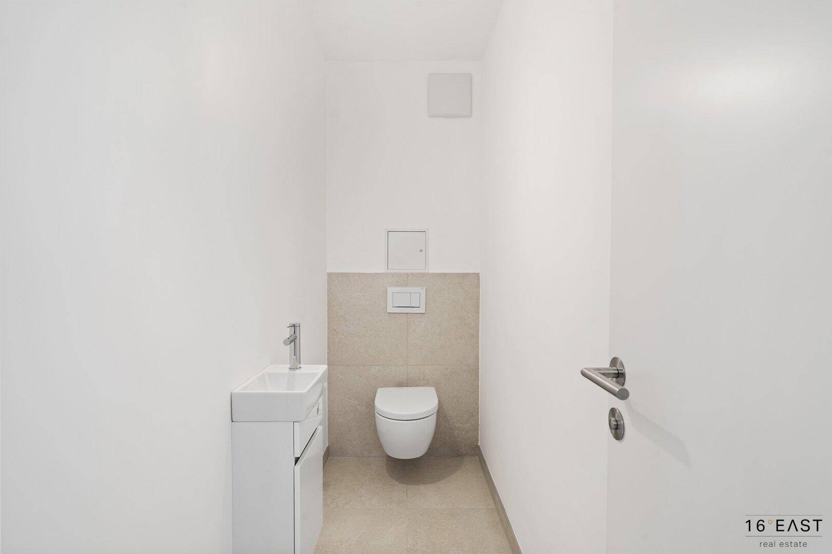 Modernes Gäste-WC mit wandhängender Toilette und kleinem Waschbecken, in schlichtem Design gehalten.