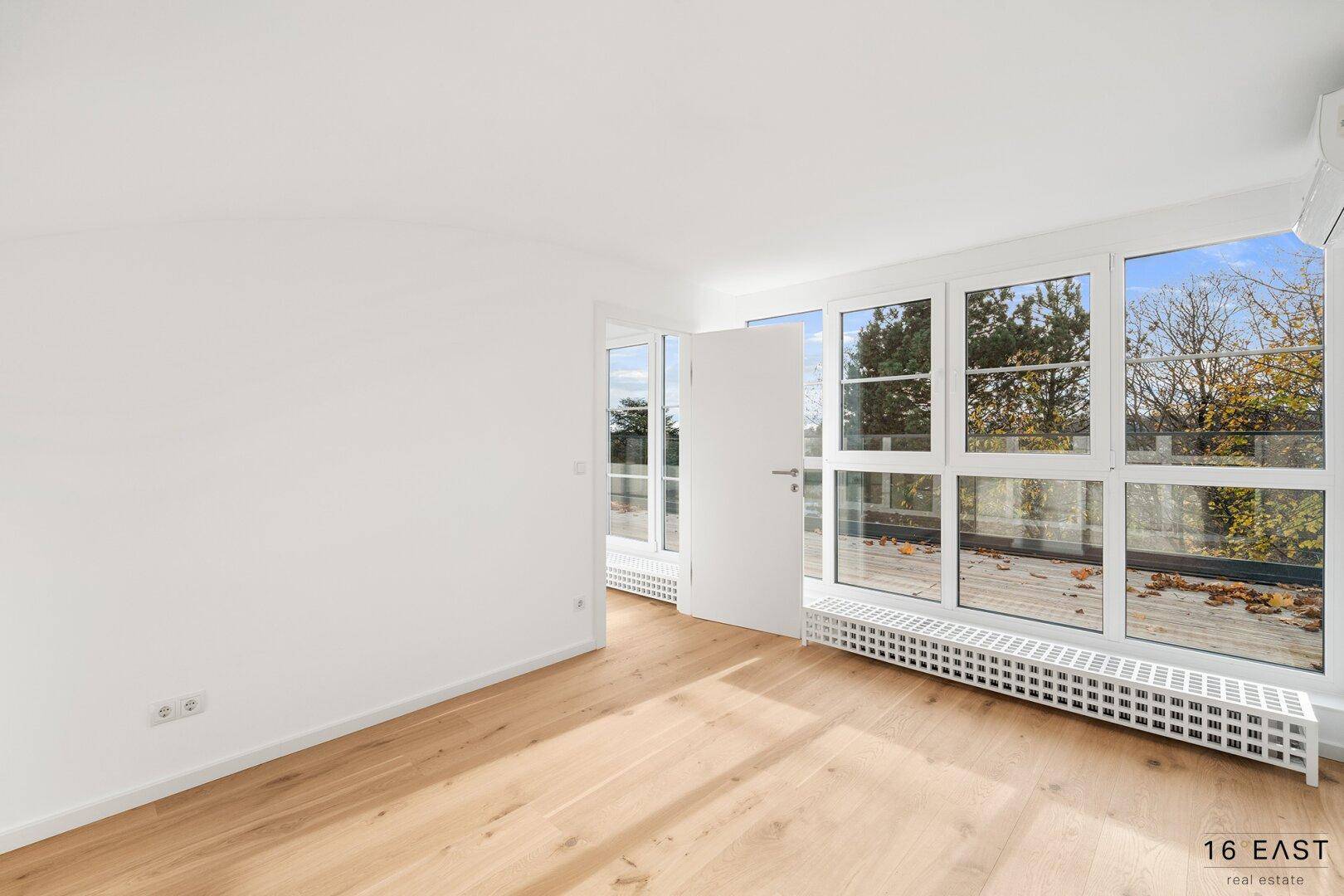 Helles Schlafzimmer mit Holzboden, großen Fenstern und Zugang zur Terrasse, bietet viel Tageslicht.