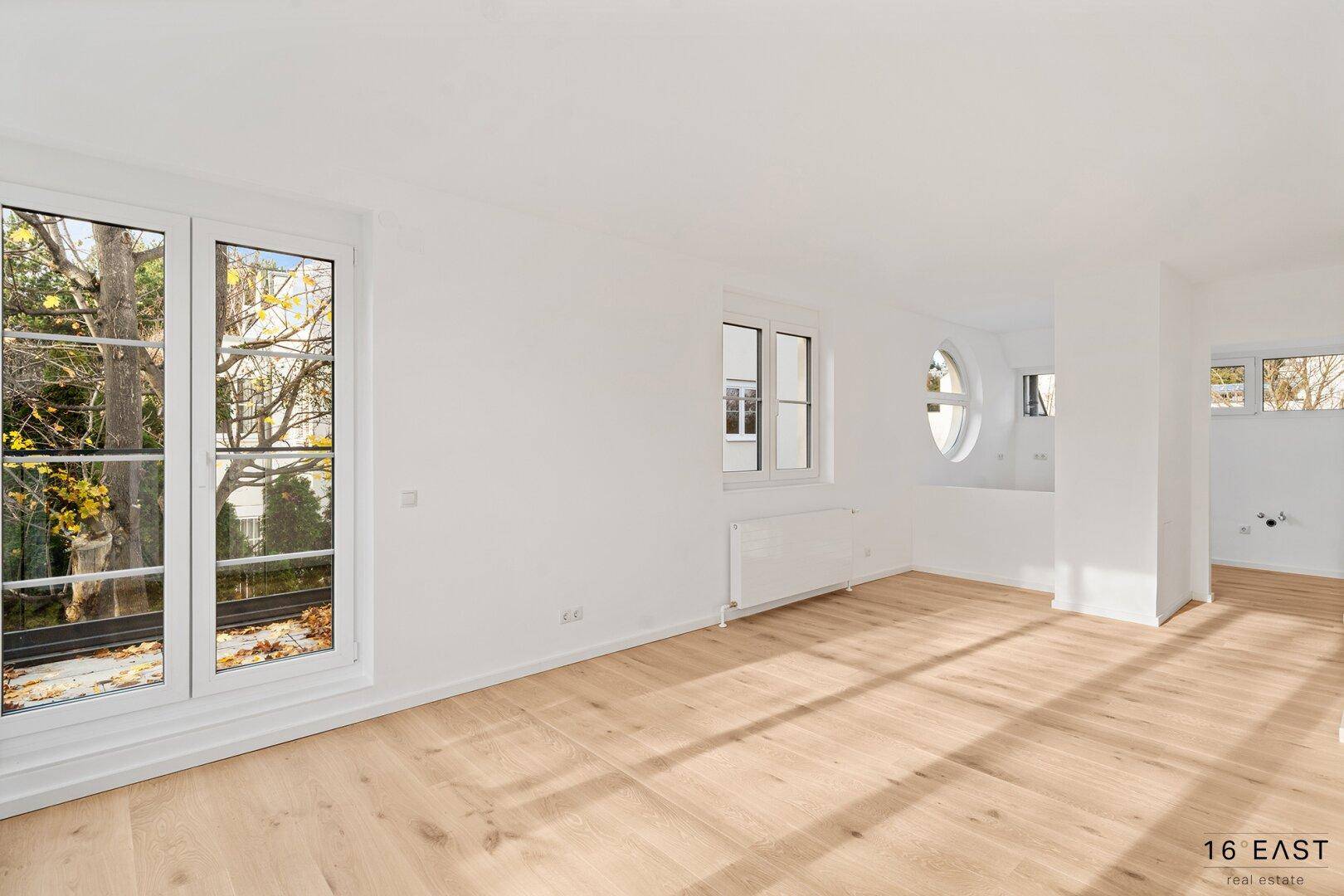 Heller Raum mit Holzboden und verschiedenen Fenstern, vorbereitet für Waschmaschinenanschlüsse.