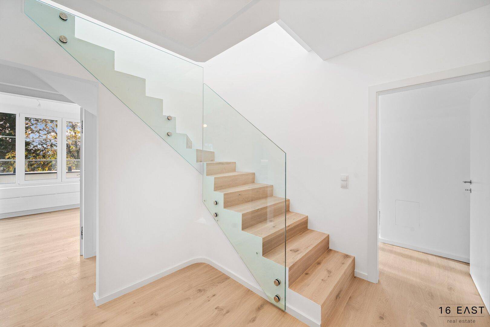 Moderner Flur mit Holzboden und eleganter Holztreppe mit Glasgeländer, verbindet die Stockwerke.