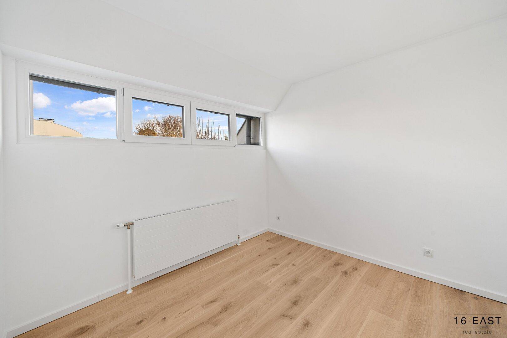 Helles Zimmer mit Holzboden und schmalen Fenstern, bietet eine ruhige und funktionale Atmosphäre.