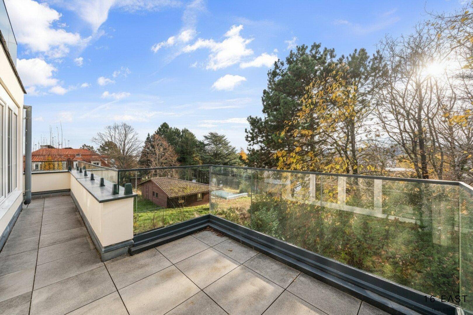 Weitläufige Terrasse mit Fliesenboden und Glasgeländer, bietet einen weiten Blick über die Umgebung und ins Grüne.