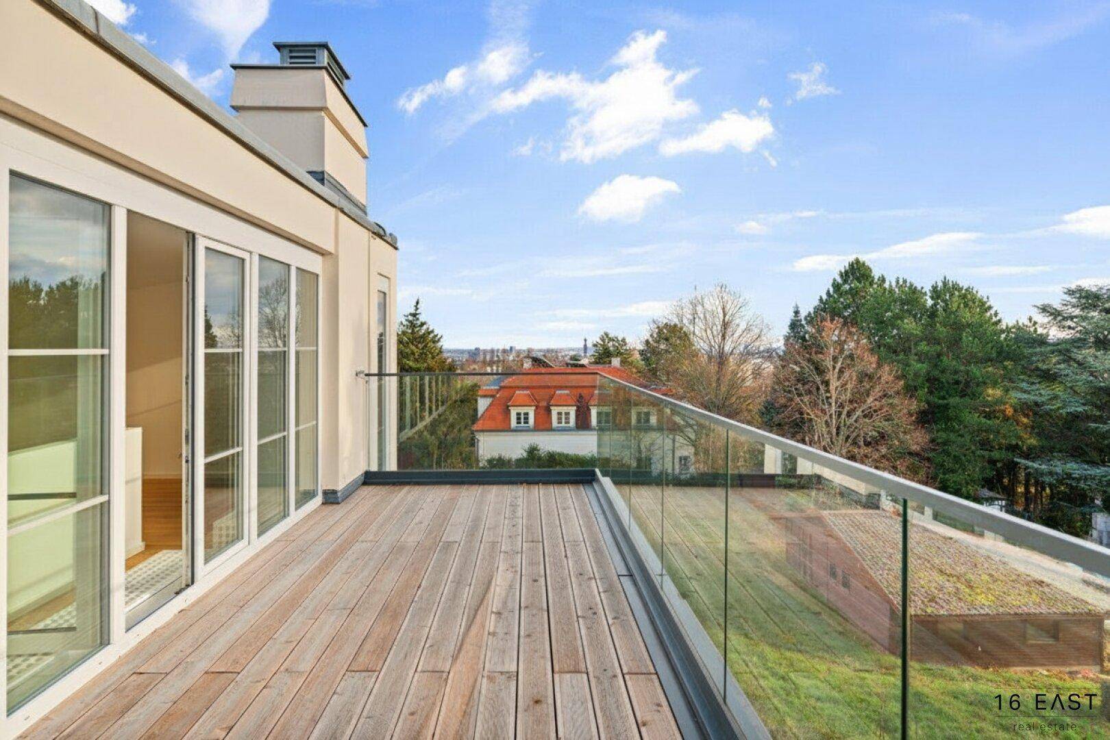 Weitläufige Holzterrasse mit Glasgeländer und Panoramablick über die Umgebung, bietet viel Platz im Freien.