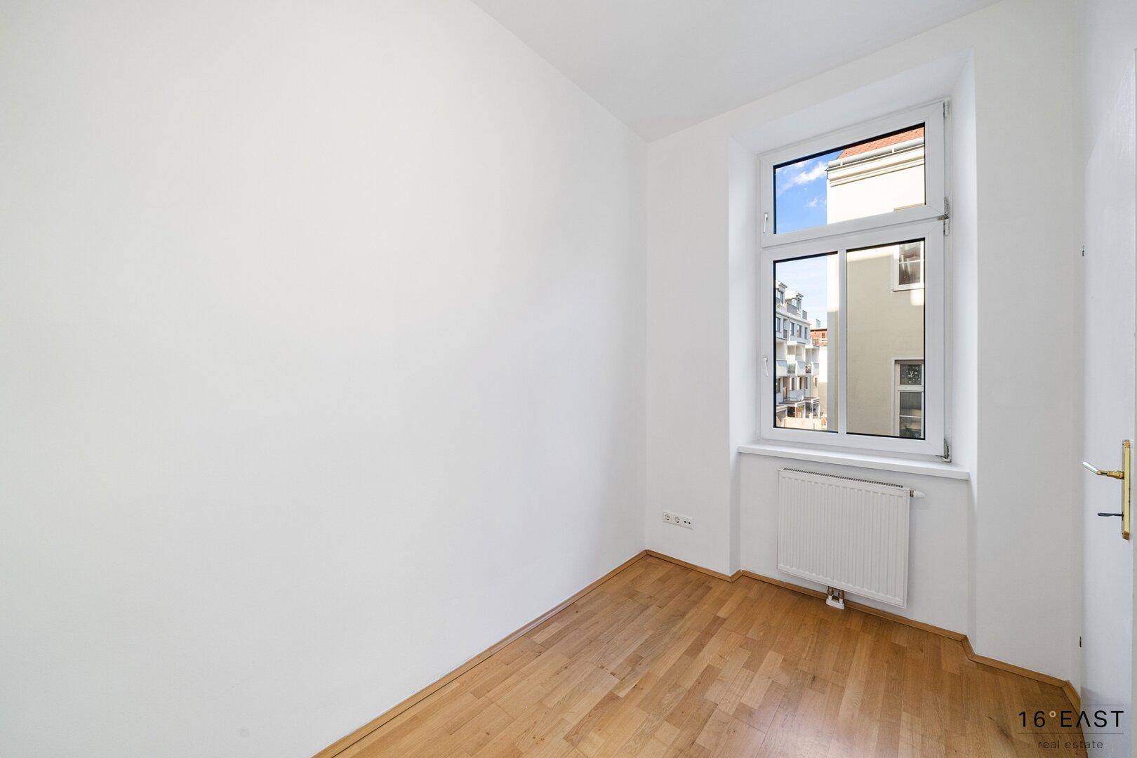 Leerer Raum mit Holzboden und Fenster, ideal als kleines Arbeitszimmer oder Kinderzimmer.